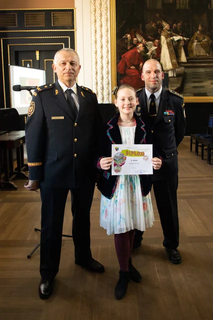 Magdaléna holding her diploma between two firefighters at the Fire Protection Through Children’s Eyes award ceremony