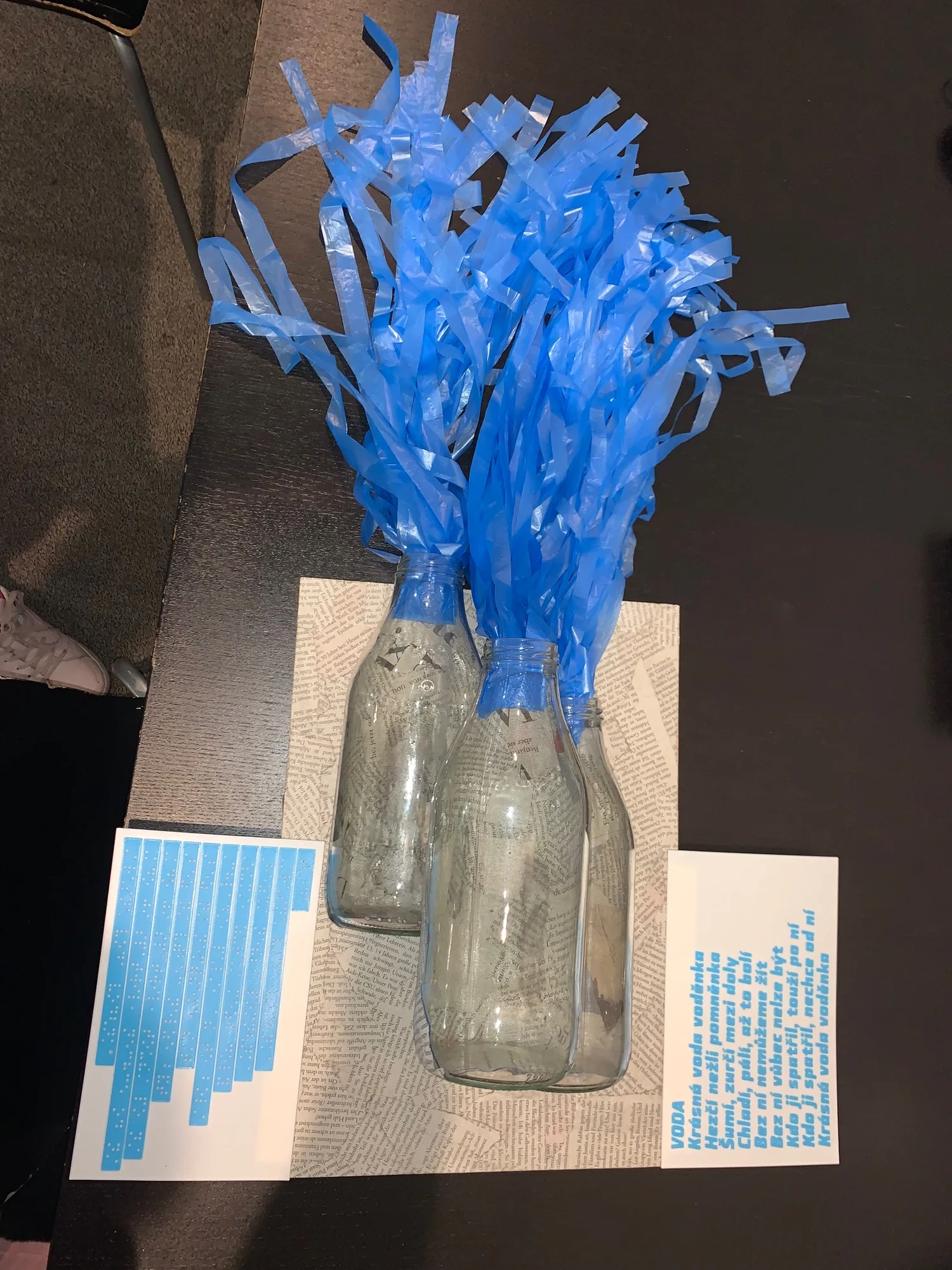 Full view of the tactile Water artwork with three glass bottles, blue ribbons and poem panels