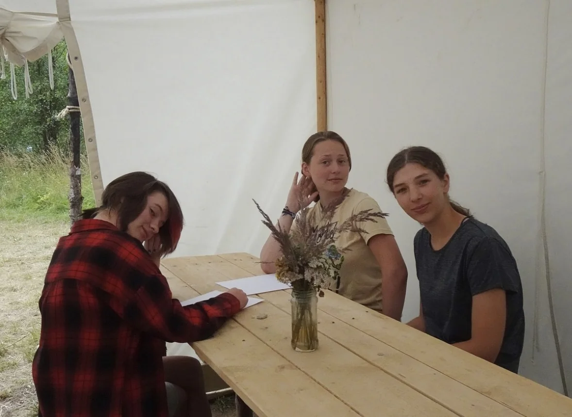Three friends sitting together at a wooden table in a Scout tent