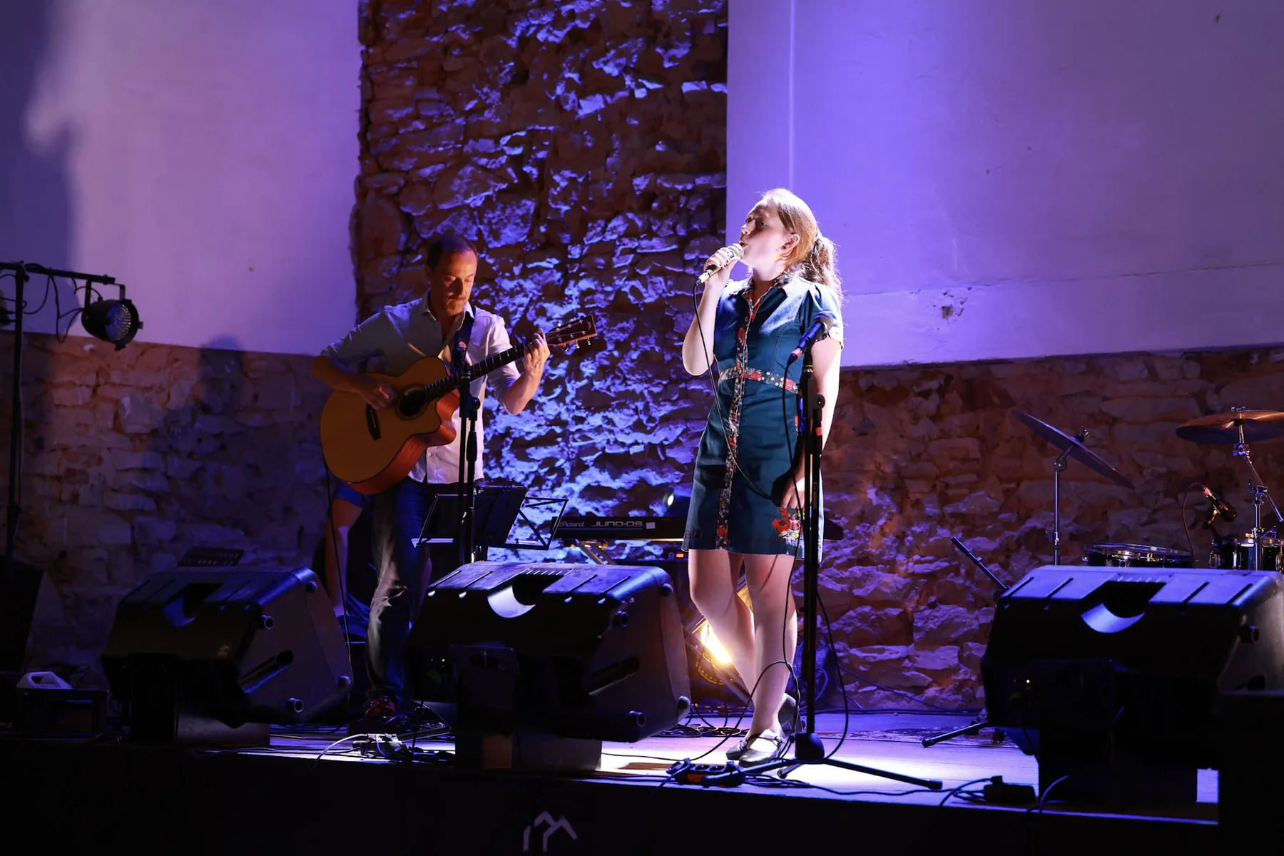 Magdaléna performing with a guitarist under violet stage lights